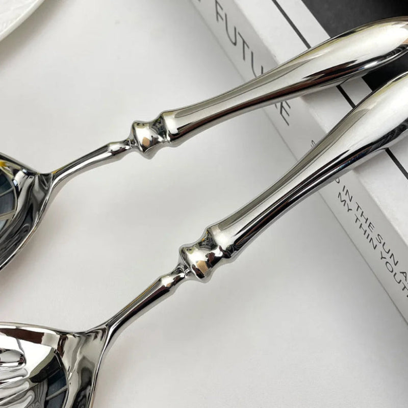A close-up of the handles of two polished silver serving spoons with an ornate, fluted design.