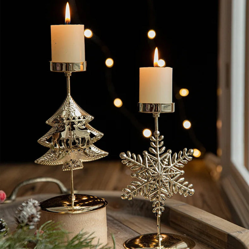 Two lit candles in gold Christmas tree and snowflake candle holders.