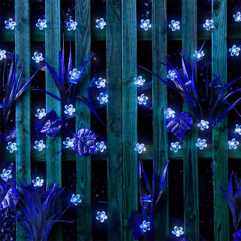 Blue LED flower lights decorating a wooden fence and plants at night.