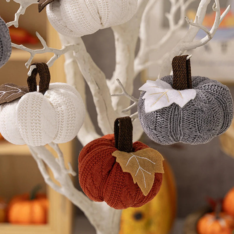 Knitted pumpkins in white, gray, and orange hang from the branches of a white decorative tree.