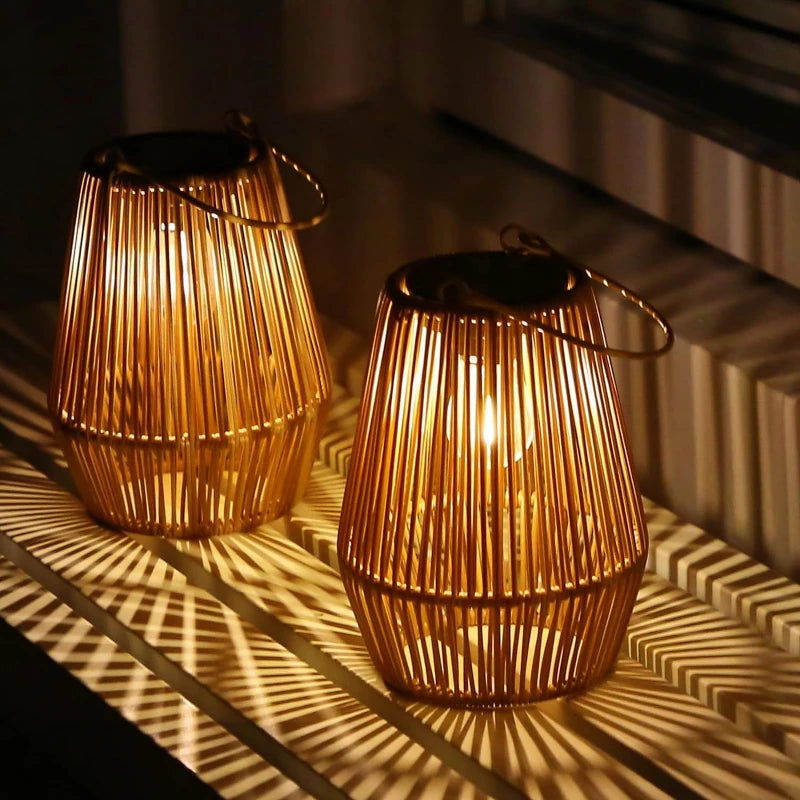 Two warm-toned, woven outdoor lanterns with vertical slats and dark tops emit a soft glow, casting striped shadows on a surface at night. Each lantern has a metal handle for hanging.