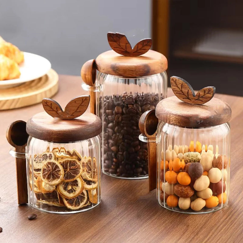 Three glass jars with wooden lids on a wooden surface, containing dried fruits and coffee beans.