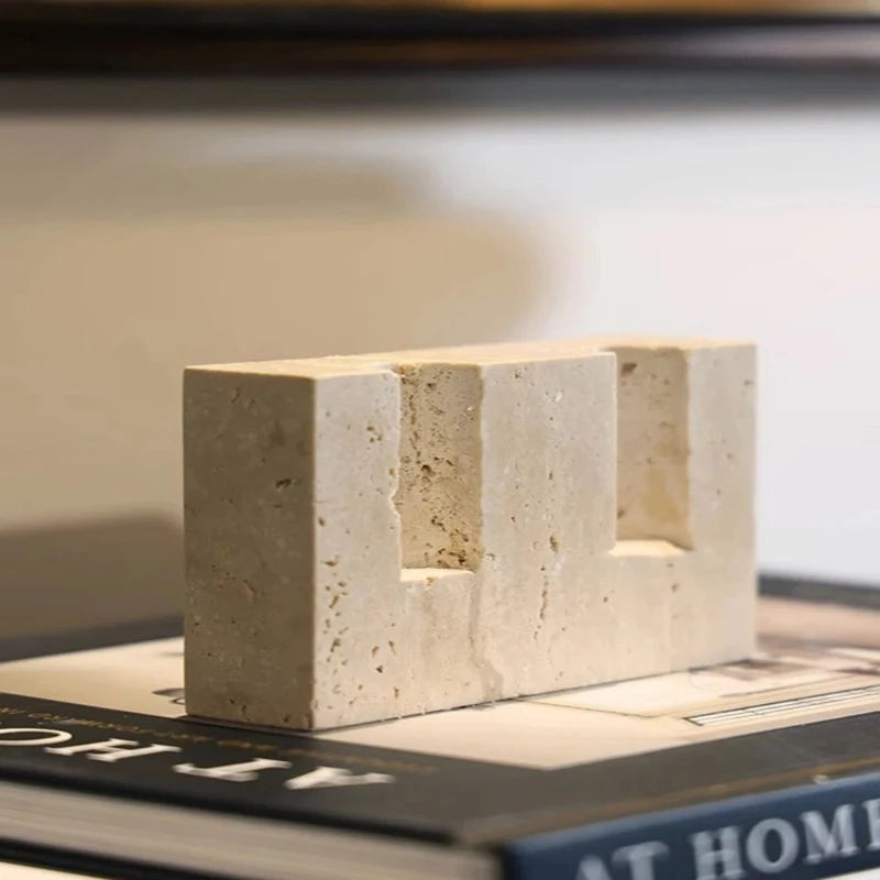 A textured, light-colored faux travertine stone block with two cylindrical openings, resting on a book.