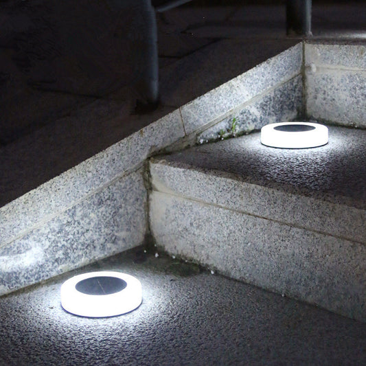 Two round, white solar pathway lights with dark centers are embedded in stone steps at night, emitting a bright white upward glow.