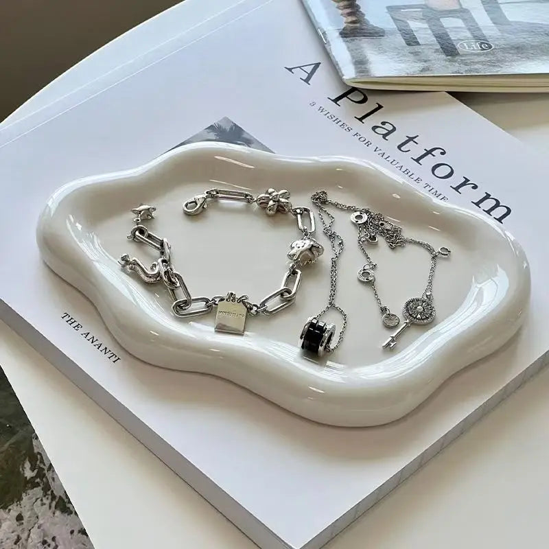 A white, irregularly shaped tray holding silver jewelry, resting on a book titled "A Platform" by "The Ananti".