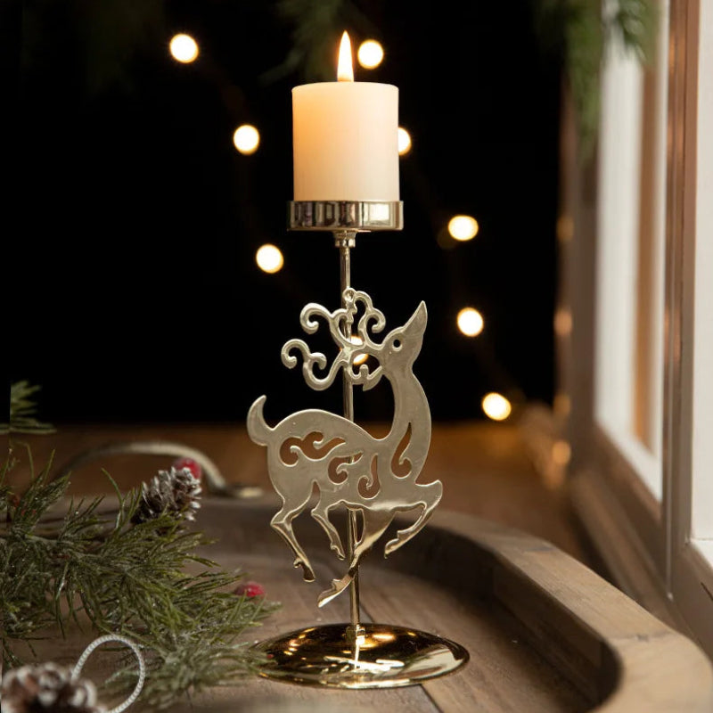 Lit candle in a gold reindeer-shaped candle holder with pine decorations.