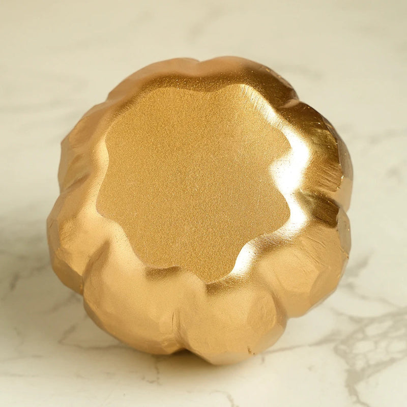 A top-down view of a small, decorative golden pumpkin with a faceted texture. The pumpkin's stem is not visible.