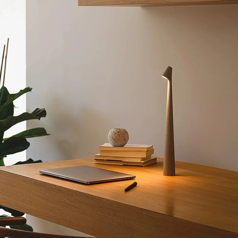 Minimalist desk setup with a laptop, books, decorative orb, and a tall, slender lamp.