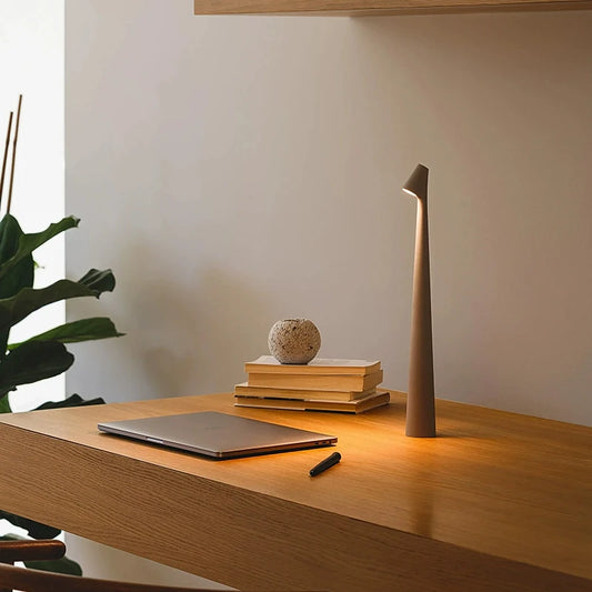 Minimalist desk setup with a laptop, books, decorative orb, and a tall, slender lamp.