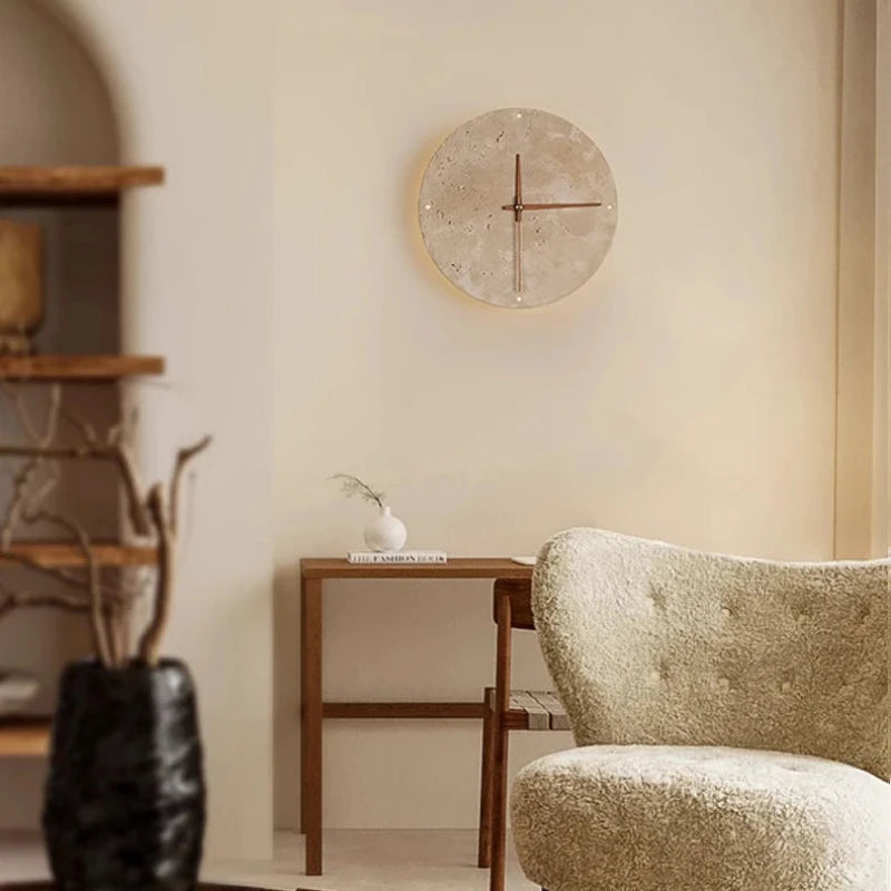 A round wall clock with a light-colored, textured face and simple red hands is mounted on a light beige wall.