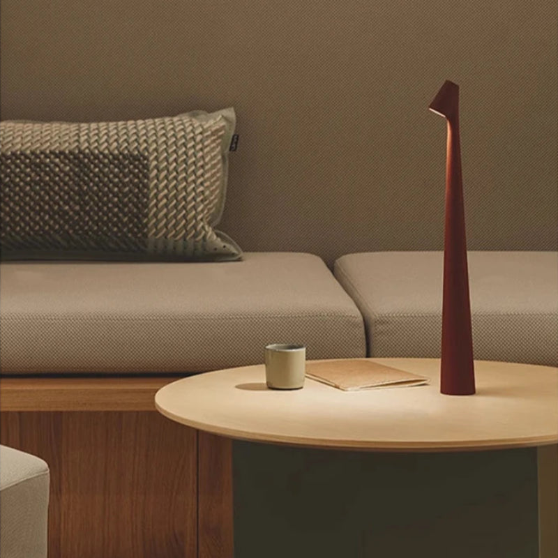 A minimalist bedside table with a uniquely shaped, tall, red lamp and a cup.