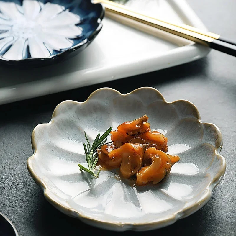 A small, light-colored, flower-shaped dish with a small serving of seafood and a sprig of rosemary.