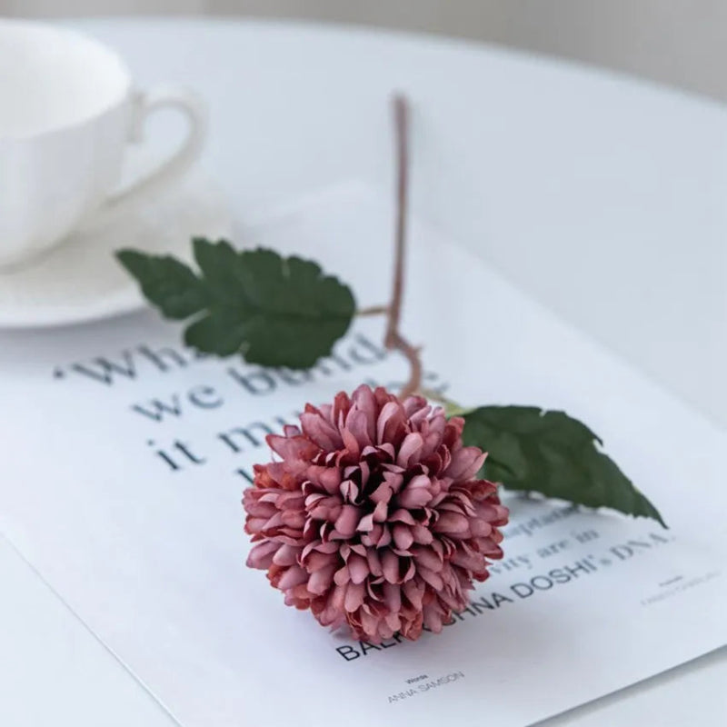 A single maroon chrysanthemum flower on a white table with a cup.