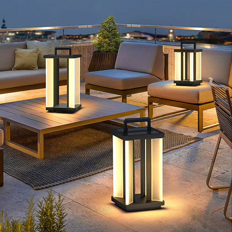 Three illuminated "Villa Solar Lamps" of different sizes are arranged on a rooftop patio with outdoor furniture at night, overlooking a cityscape.
