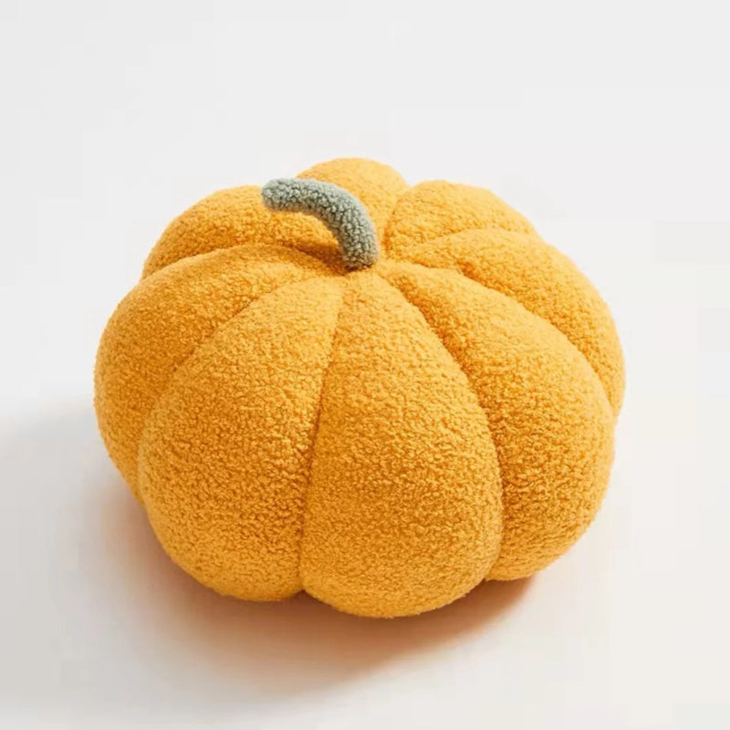 A plush, textured, yellow pumpkin-shaped pillow with a light green stem sits on a clean white surface.