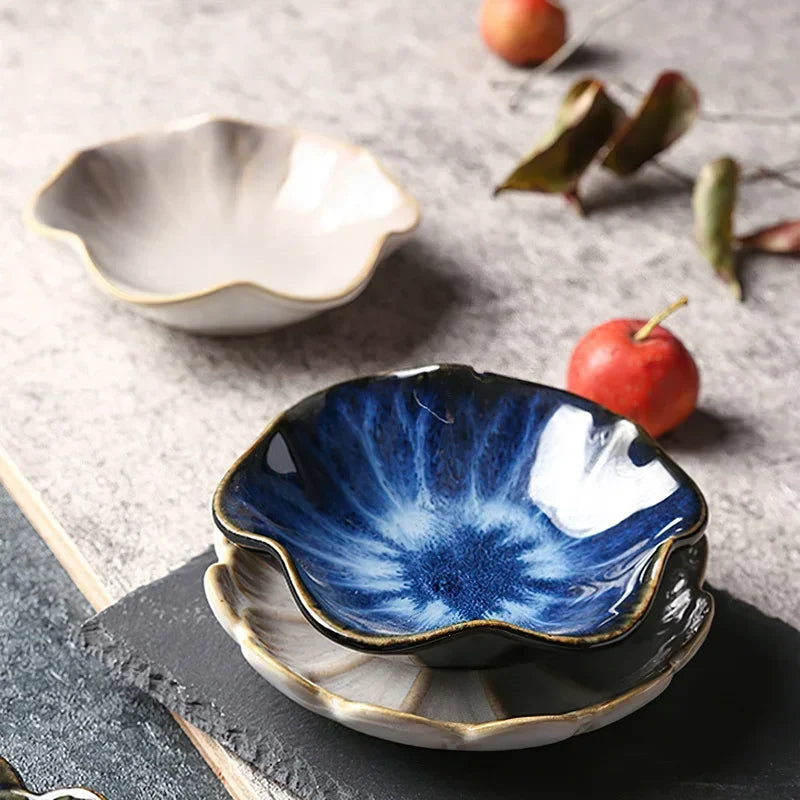 Two stacked, flower-shaped condiment dishes, one blue and one white, with a third white dish in the background.