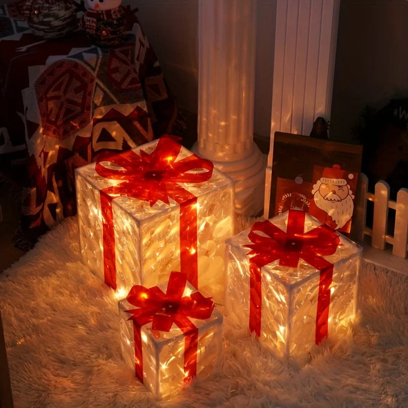 Three clear, illuminated gift boxes with red bows sit on a fluffy white rug, casting a warm glow in a dimly lit room decorated for Christmas.