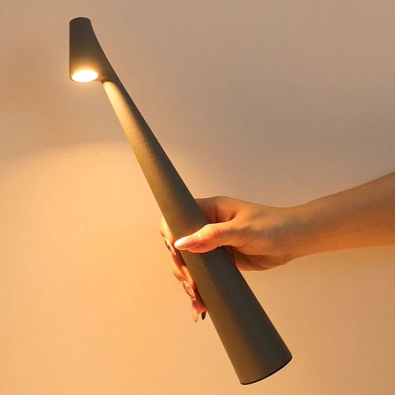 A hand holding a sleek, dark gray portable lamp with a warm light.