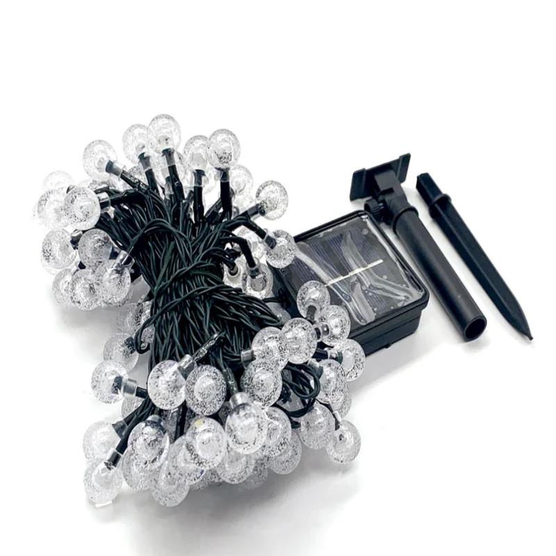 A tangled string of clear, round, textured lights with a black wire is shown next to a black solar panel and two black ground stakes on a white background.