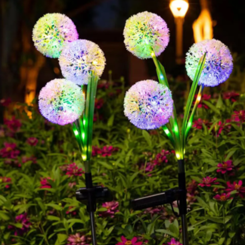 Six colorful solar dandelion lights illuminate a garden at night.