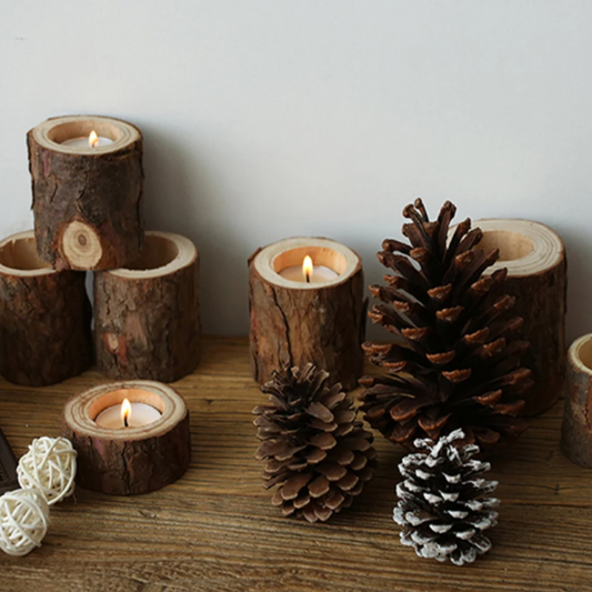 Rustic wooden candle holders made from logs, each with a lit tea light, are arranged with scattered pinecones.