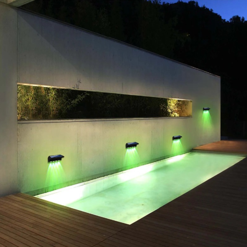 Four solar-powered fence lights are mounted along a low wall, illuminating a wooden walkway at dusk or night. The lights cast beams downwards onto the path.