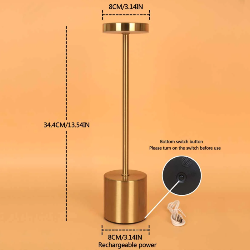 A cordless LED table lamp with a brushed gold finish is shown against a solid orange background with dimensional measurements and a detail of the bottom switch and charging port. The lamp has a cylindrical base with a diameter of 8cm/3.14in, a total height of 34.4cm/13.54in, and a circular light panel at the top with a diameter of 8cm/3.14in. Text indicates a "Bottom switch button" that needs to be turned on before use, and labels the charging port as "Rechargeable power." A charging cable is also visible.