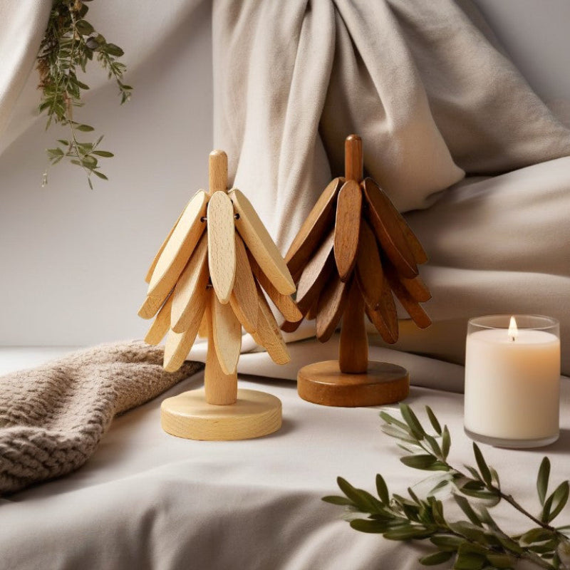 Two tree-shaped wooden trivets, one light and one dark, sit on a textured surface with a lit candle nearby.