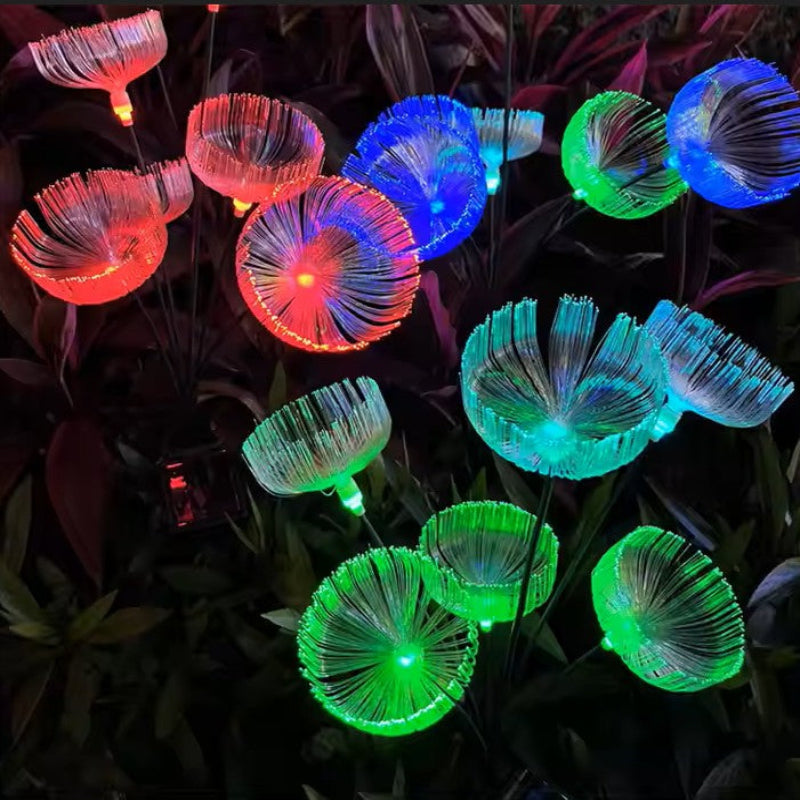 Several solar-powered garden lights with a jellyfish-like shape emit a vibrant mix of red, blue, and green glows in a garden at night, standing among dark foliage.