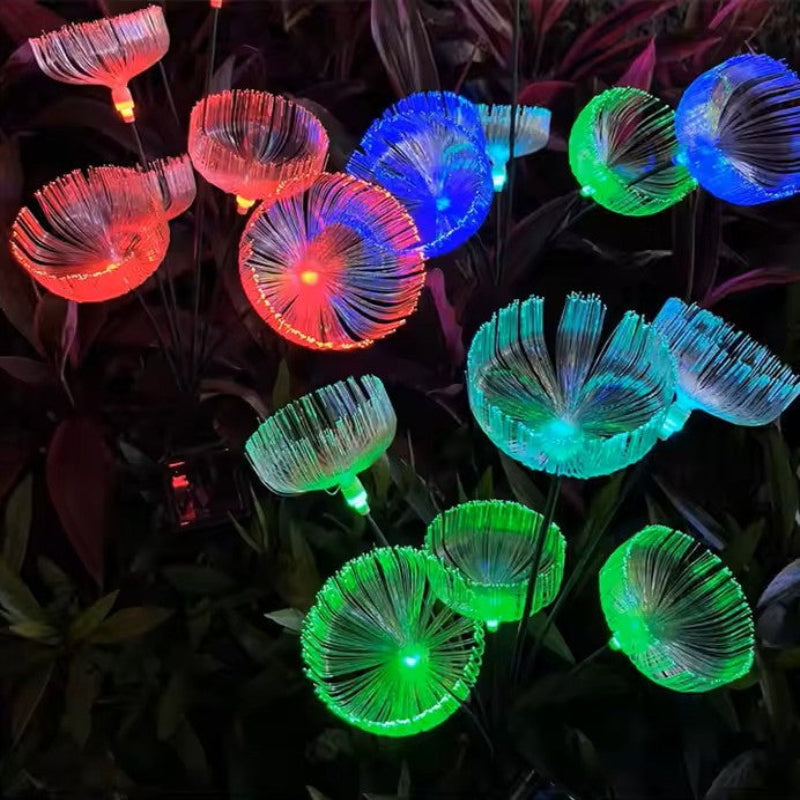 Several solar-powered garden lights with a jellyfish-like shape emit a vibrant mix of red, blue, and green glows in a garden at night, standing among dark foliage.