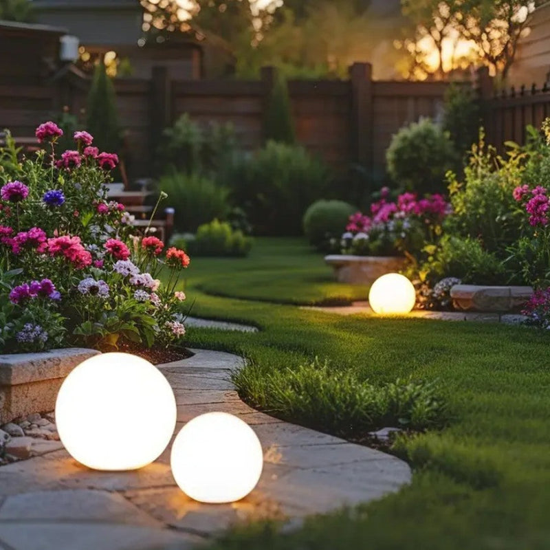 Glowing spherical garden lights in a well-maintained garden with flowers and a wooden fence.