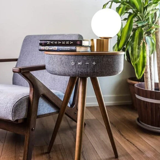 Small round side table with wooden legs next to a chair, featuring books and a lamp.