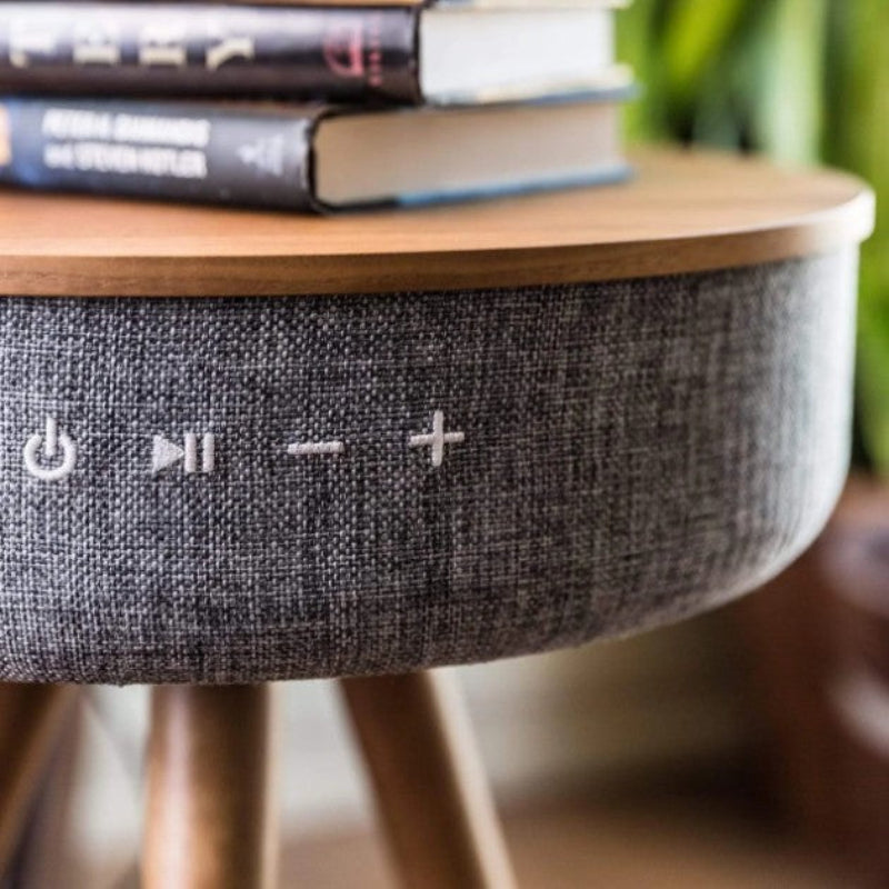 Round wooden table with a textured gray base featuring control buttons, stacked books on top.