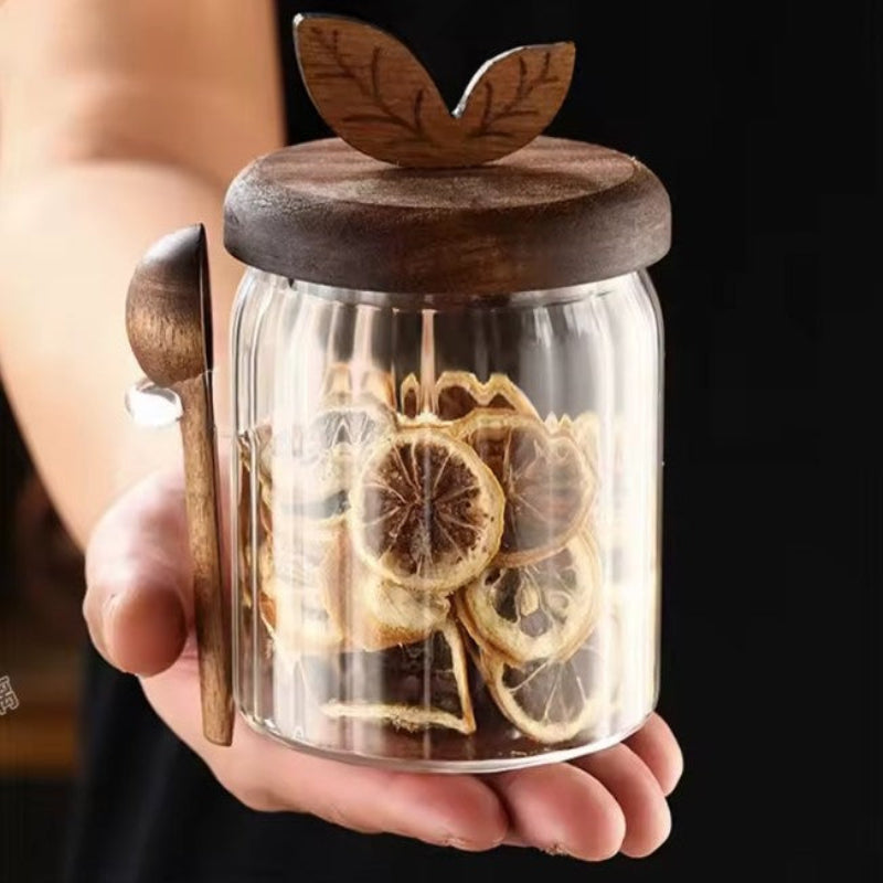 Glass jar with wooden lid and decorative elements, held by a person against a dark background