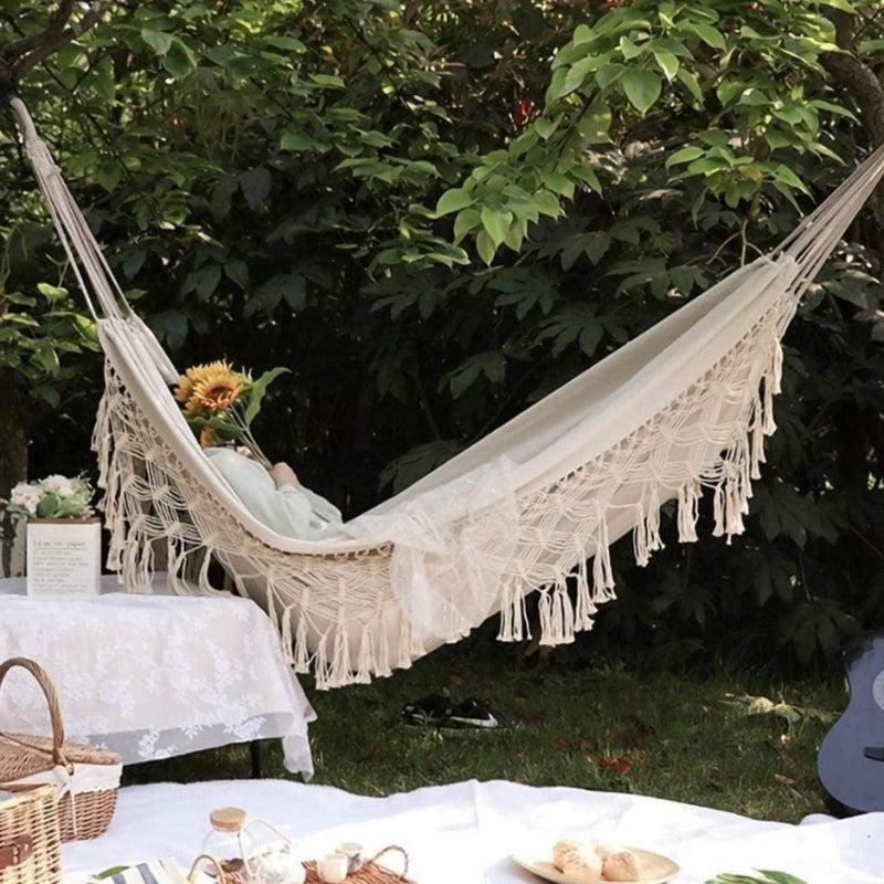 Beige hammock with tassels in a garden setting with a table and picnic setup.