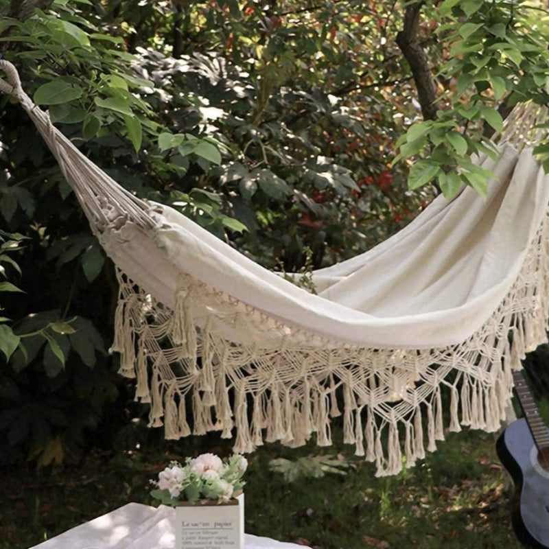White hammock with tassels hanging in a garden setting