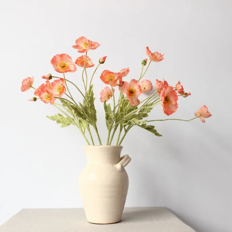 A cream-colored vase with handles holds a bouquet of orange poppies.