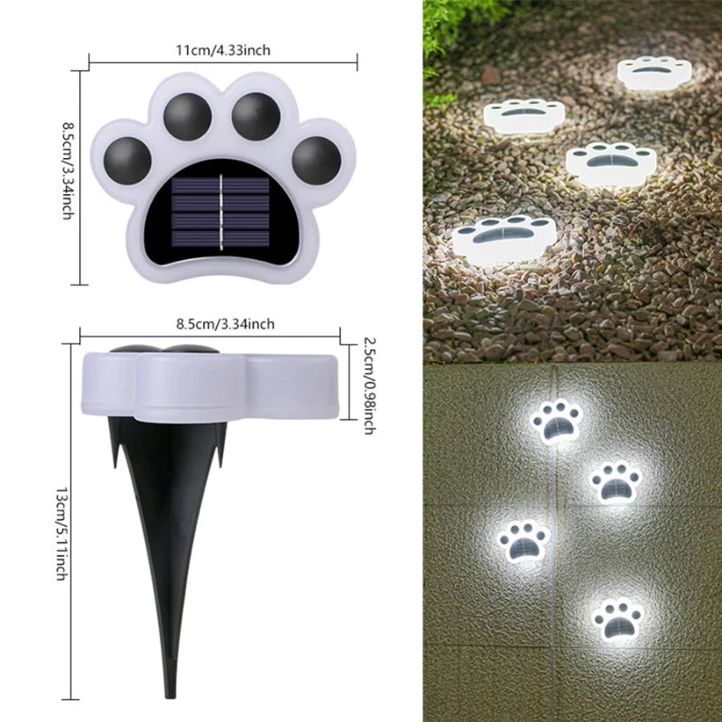 A composite image displays diagrams detailing the dimensions of a white, paw-shaped solar ground light with black paw pads and a central solar panel. The diagrams show the light's width as 11 cm/4.33 inches, paw height as 8.5 cm/3.34 inches, stake height as 13 cm/5.11 inches, and head thickness as 2.5 cm/0.98 inches. Additionally, the image features examples of these lights illuminating outdoor spaces at night, creating a paw print pattern on gravel and a textured surface with a warm glow.