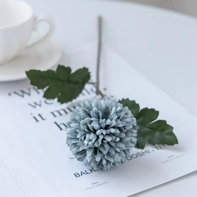 A single light blue chrysanthemum flower on a white table with a cup.