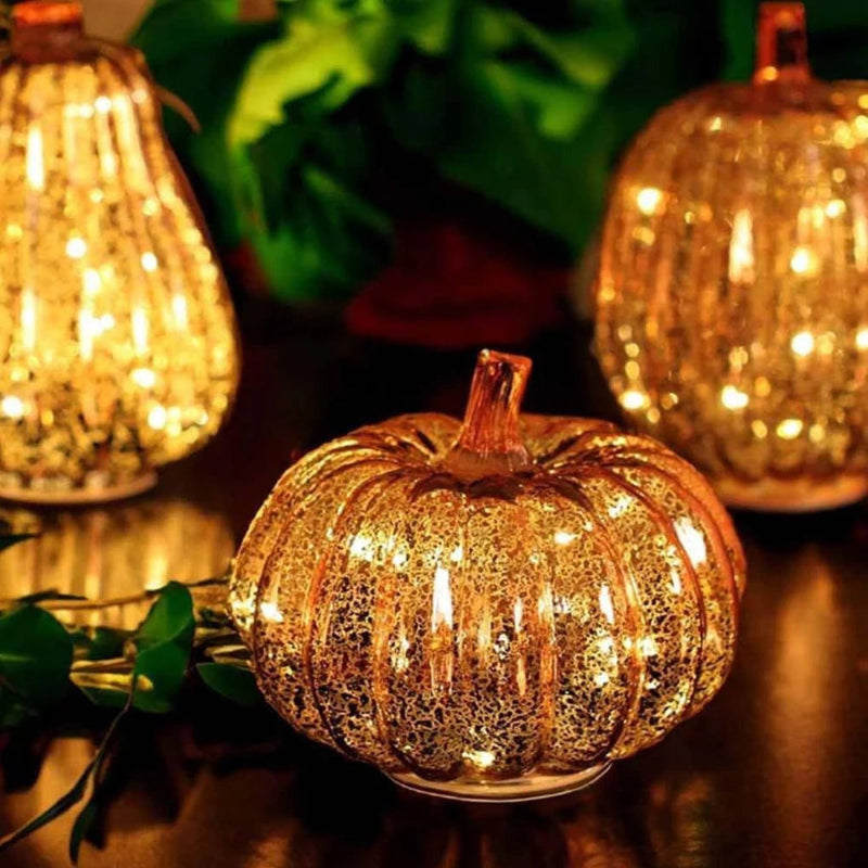 A close-up of a small, glowing, gold-colored pumpkin decoration with lights, with two other similar pumpkins in the blurred background.