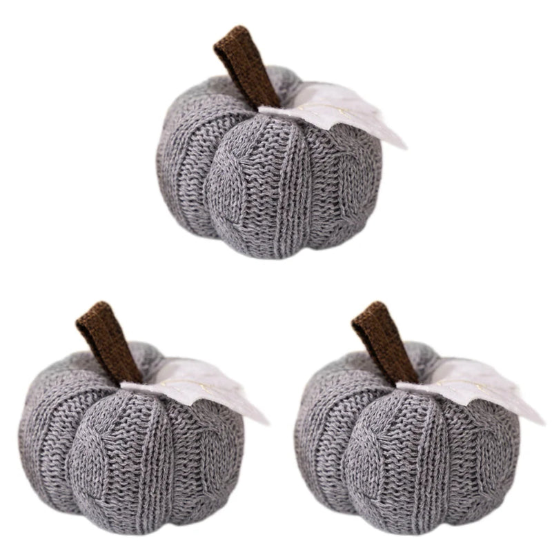 Three identical gray knitted pumpkins, each with a brown stem and a white leaf, are arranged on a white background.