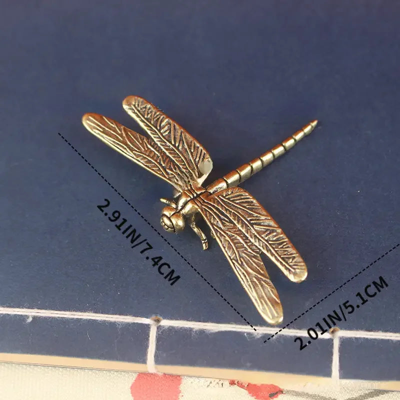 Bronze dragonfly-shaped object with measurements on a blue background