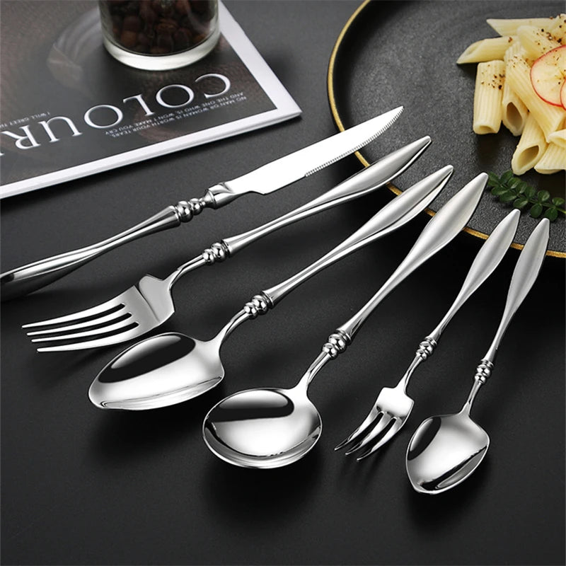 A set of silver utensils, with a plate of pasta in the background.
