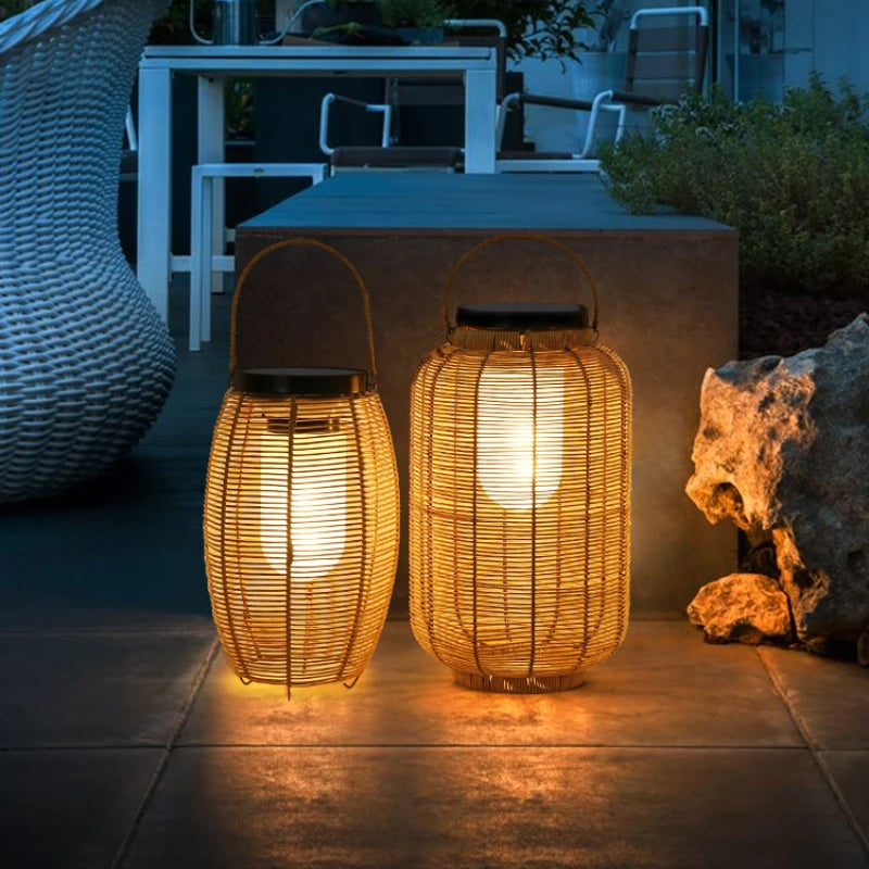 Two warm-toned, cylindrical outdoor lanterns made of vertical slats emit a soft glow as they sit on a surface. The lanterns have handles for hanging.