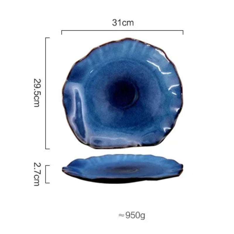 Top and side views of a large, glossy, deep blue ceramic plate with an irregular edge are shown against a white background. The top view indicates a maximum width of 31 cm and a maximum length of 29.5 cm. The side view shows a height of 2.7 cm. The approximate weight is 950g.