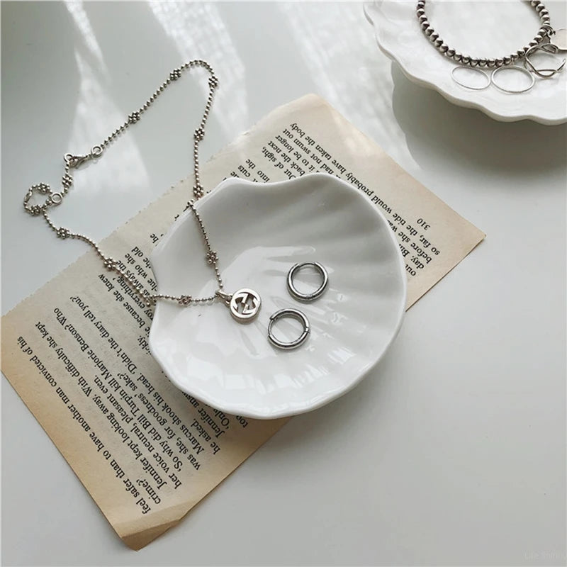 Silver jewelry in a white shell-shaped dish on a piece of paper.