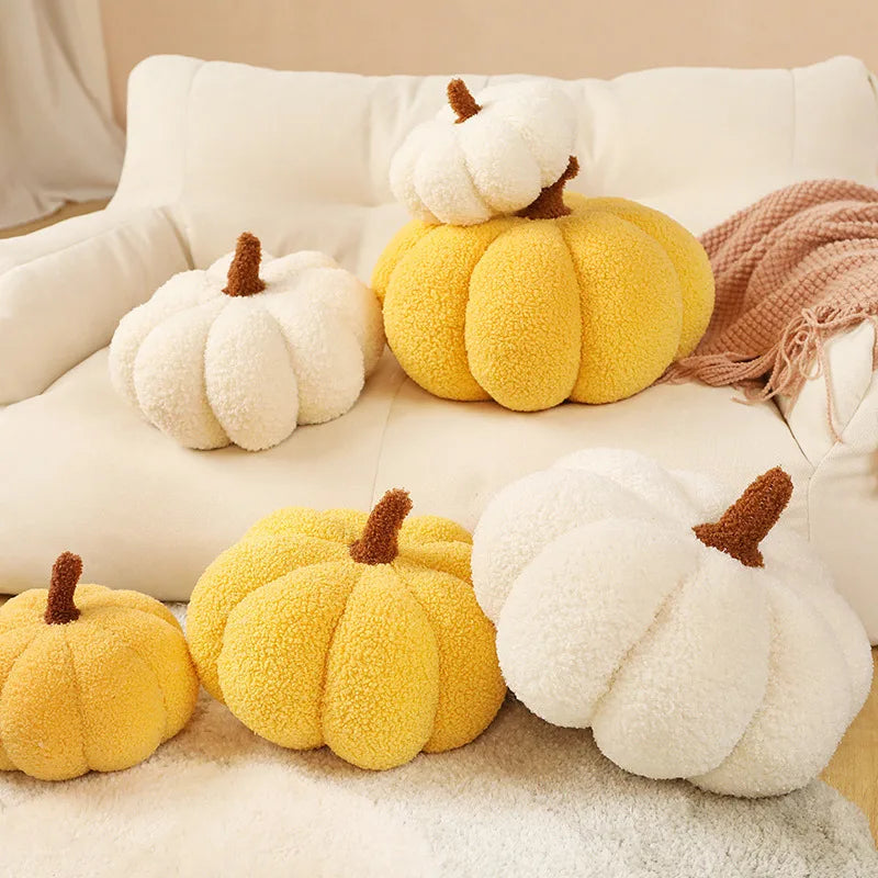 A group of white and yellow pumpkin-shaped pillows are displayed on a white sofa and a rug, with one smaller white pumpkin pillow stacked on top of a larger yellow one.