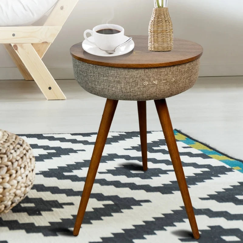 A wooden end table with three legs and a built-in Bluetooth speaker, topped with a cup of coffee and a vase.