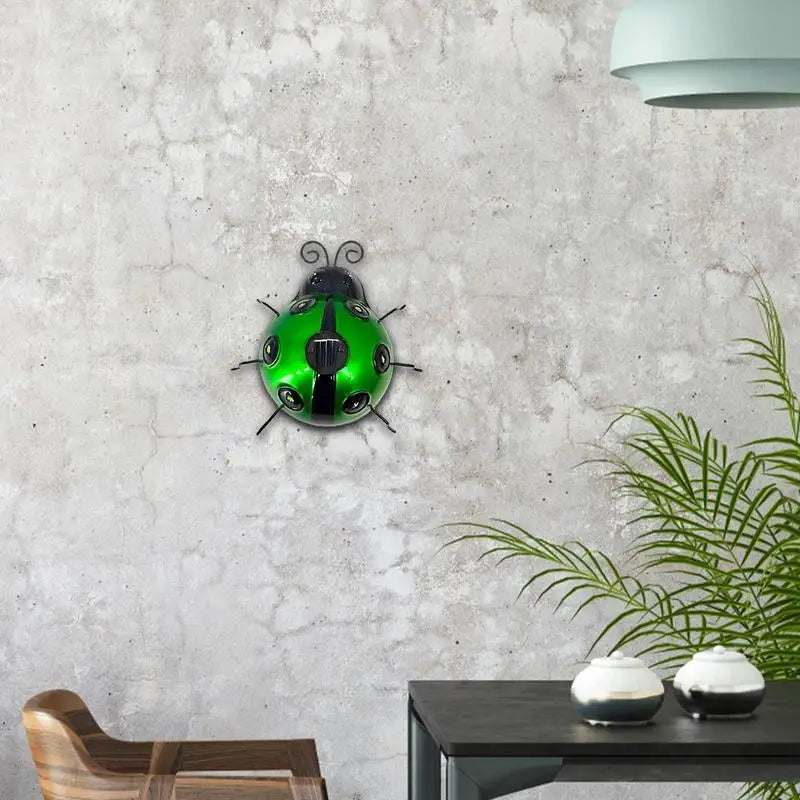 A decorative green metal ladybug with black accents is mounted on a textured light gray wall. A wooden chair, a black table with two small white containers, and a potted palm are partially visible in the room.