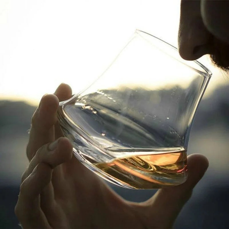 A person savoring the aroma of whiskey from a uniquely shaped glass, designed to enhance the tasting experience, against a softly lit background.